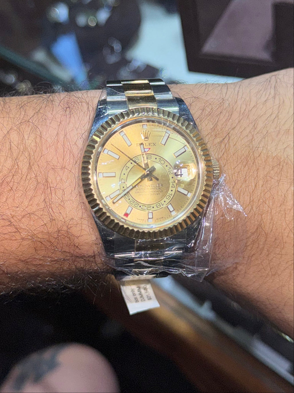 A two-tone gold and stainless steel wristwatch with a gold dial, worn on a person's wrist inside what appears to be a jewelry store.