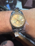 A two-tone gold and stainless steel wristwatch with a gold dial, worn on a person's wrist inside what appears to be a jewelry store.