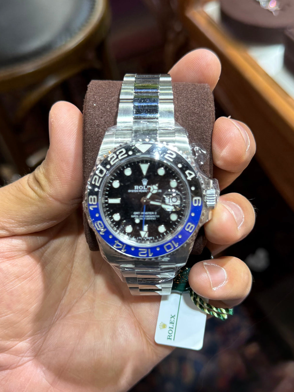 A silver stainless steel wristwatch with a black dial and blue bezel, held in a person's hand inside what appears to be a jewelry store.