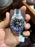 A silver stainless steel wristwatch with a black dial and blue bezel, held in a person's hand inside what appears to be a jewelry store.